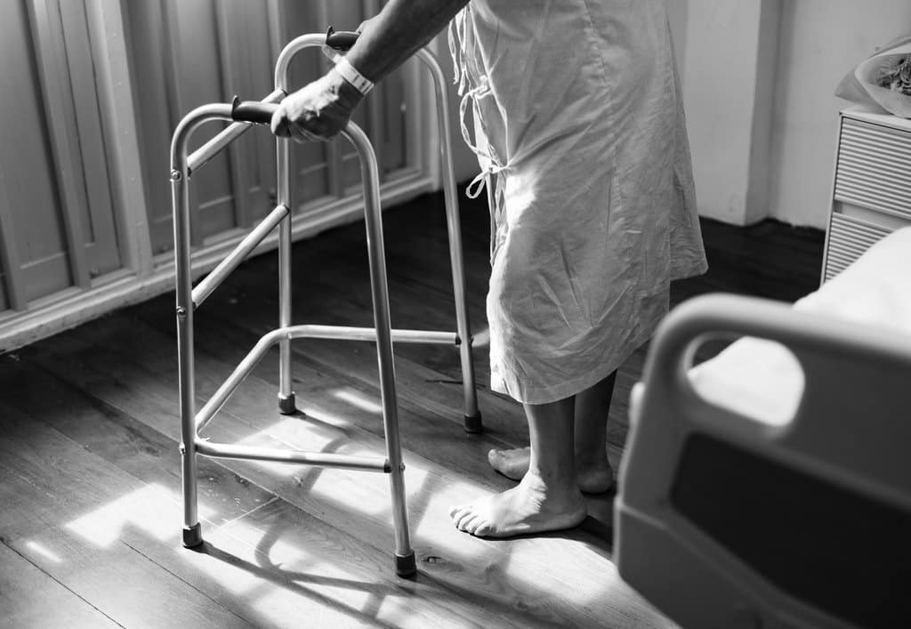Crno bijela slika osobe oboljele od multiple skleroze s hodalicom.