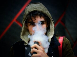 Čovjek s kapuljačom puši e-cigaretu s CBD e-tekućinom.