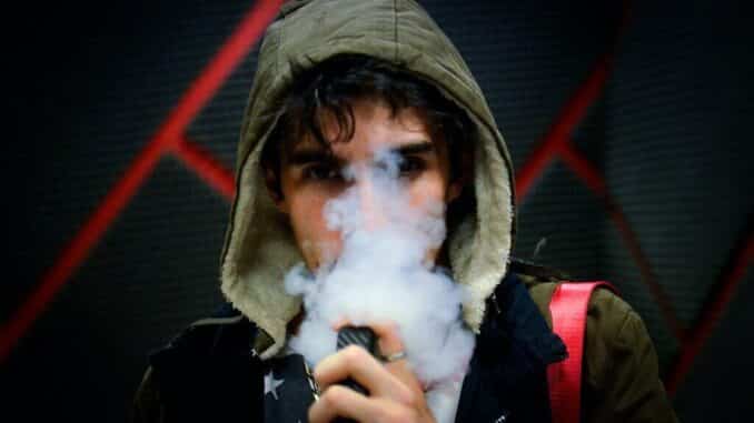 Čovjek s kapuljačom puši e-cigaretu s CBD e-tekućinom.